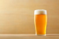 Fresh cold lager beer with foam head in traditional pint glass against wooden background, condensation droplets on glass surface, minimalist composition.