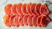 Fresh raw pork loin slices arranged in rows on light marble background, showing meat texture and marbling pattern for culinary and food photography.