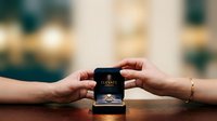 Hands exchanging luxury fragrance box with gold accents on wooden surface, elegant gift presentation for perfume marketing, cosmetics advertising, and retail product promotion.