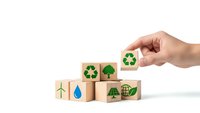 Hand placing wooden cube with recycling symbol among eco-friendly blocks featuring green energy icons on white background for sustainable business concepts.