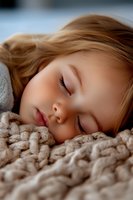 Peaceful sleeping young girl with blonde hair resting on cozy knitted blanket, soft natural lighting creates gentle atmosphere for childhood, parenting and lifestyle designs.