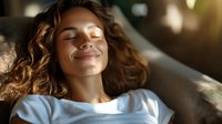 Young woman with curly hair relaxing on couch with eyes closed and peaceful smile, enjoying mindful moment in warm sunlight streaming through window.