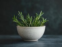 Fresh rosemary sprigs in ceramic bowl against dark background, aromatic herbs for cooking and natural food styling. Minimalist kitchen composition.