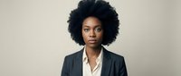Professional African American businesswoman with natural afro hairstyle wearing dark blazer and white shirt against neutral background for corporate use.