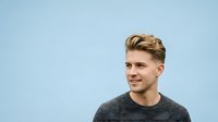 Young man with blonde hair and fair complexion wearing gray crew neck sweater against light blue background, suitable for corporate portraits, business profiles, and professional headshot applications.