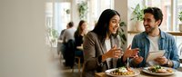Young diverse couple enjoying lunch date at modern restaurant sharing meal and conversation while smiling together in bright casual dining atmosphere.