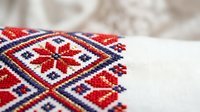 Traditional folk embroidery with red and blue geometric patterns on white linen fabric, showcasing handmade cross-stitch ornamental design.