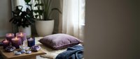 Cozy bedroom interior with purple pillow, burning candles, plants and soft natural lighting creating peaceful relaxation atmosphere for wellness.