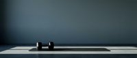 Minimalist workspace with two black cylindrical objects on white desk against dark gray wall background.
