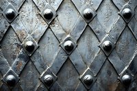 Antique metal door surface with diamond pattern and round rivets, featuring weathered gray steel texture with rustic patina and geometric design details.