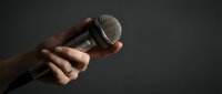 Hand holding professional microphone against dark background for broadcasting, podcasting, music recording, and live performance applications.