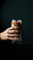 Hand holding tall glass of cola with ice cubes against dark background. Refreshing beverage concept for advertising, restaurant menus, and drink promotions.