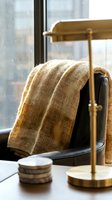 Cozy beige knitted blanket draped over black leather chair with brass lamp in warm natural light interior setting for home comfort and relaxation.