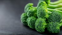 Fresh raw broccoli florets macro view on dark background. Healthy green vegetable with detailed texture showing tiny buds in natural lighting.