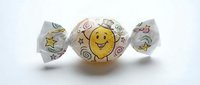Wrapped candy with cheerful yellow smiley face character and decorative swirls on white twisted cellophane wrapper, suitable for confectionery packaging and candy design projects.