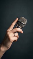 Male hand holding professional microphone against dark background for broadcasting, podcasting, music recording, and live performance applications.