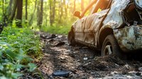 Abandoned rusty car wreck in green forest with sunlight streaming through trees, stuck in muddy ground. Environmental damage concept for nature conservation.
