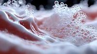 Macro photography of soap bubbles and foam creating abstract texture in pink and white tones against dark background, showing delicate surface tension patterns.