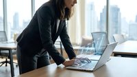 Professional businesswoman working on laptop in modern office with city skyline view. Corporate executive analyzing data and reports at workplace.