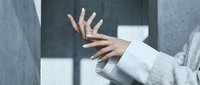 Businesswoman with manicured nails wearing white blazer gesturing against modern concrete wall background for corporate communication and professional concepts.