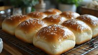 Fresh baked dinner rolls with golden brown tops cooling on wire rack in kitchen. Homemade bread buns ready for serving at family meal or holiday gathering.