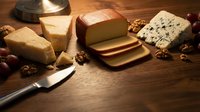 Gourmet cheese platter with aged varieties, walnuts and knife on rustic wooden board for culinary presentations and food photography.