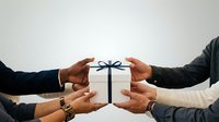 White gift box with dark blue ribbon held by four diverse hands in business attire, symbolizing teamwork, collaboration, and corporate gifting for partnership and success concepts.