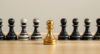 Golden chess pawn standing out among black pawns on wooden surface, representing leadership, uniqueness and strategic thinking in business concepts.