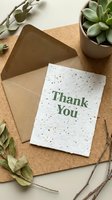 Eco-friendly thank you card with kraft envelope on cork board, surrounded by green plants and twigs, perfect for sustainable gifting.