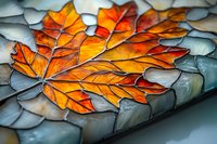 Stained glass maple leaf pattern in vibrant orange and yellow hues against cool blue-gray background creates dramatic autumn seasonal contrast and artistic detail.