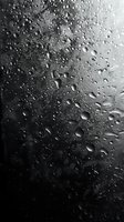 Water drops on dark glass surface creating abstract pattern with light reflection and bokeh effect in monochrome style. Suitable for mood and atmosphere designs.