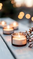 Lit candles in glass holders arranged on wooden surface with dried botanicals and warm bokeh lights, creating cozy ambiance for home decor, events, and relaxation settings.