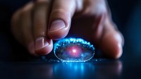 Glowing blue crystal lens held between fingers against dark background creates magical ethereal effect with light reflections and sparkles.