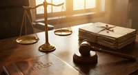 Wooden gavel and scales of justice on lawyer desk with legal documents in warm sunlight for courtroom and law firm concepts.