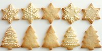 Festive sugar cookies shaped as snowflakes and Christmas trees decorated with white royal icing on white background, homemade holiday baking treats.