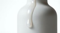 Pouring milk or cream into white ceramic bottle on isolated background, suitable for dairy product packaging and advertising designs.