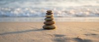 Zen stone stack balanced on sandy beach with soft ocean waves in background creating peaceful meditation and mindfulness concept for wellness and relaxation.