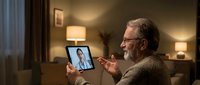 Senior Caucasian man with beard and glasses having video call consultation with female doctor on tablet in cozy living room for telemedicine healthcare.