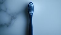 Blue plastic toothbrush with soft bristles on marble surface in minimalist composition, dramatic lighting creates modern healthcare concept for dental hygiene.