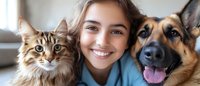 Young woman with brown hair smiling between fluffy tabby cat and German Shepherd dog in cozy home setting. Pet owner bonding with beloved animals indoors.