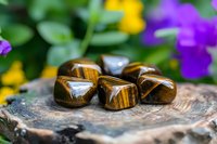 Polished tiger's eye stones on rustic wooden surface with colorful spring flowers in background creating spiritual healing atmosphere for meditation and crystal therapy.