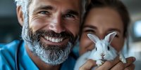Mature bearded man and woman holding white pet rabbit, showing genuine joy and connection with their furry companion. Close up portrait in natural lighting.