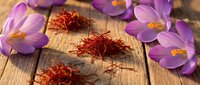 Saffron spice threads with purple crocus flowers on rustic wooden background for culinary and cooking applications.