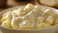 Creamy macaroni and cheese pasta with black pepper in white bowl, close up view of comfort food with rich sauce and shell shaped noodles.