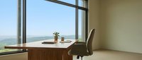 Wooden desk with office chair positioned by large window overlooking scenic landscape valley view, modern workspace interior design for remote work and business environments.