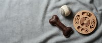 Flat lay of pet toys on soft gray fabric, featuring a leather bone, tennis ball, and wooden puzzle toy with copy space.
