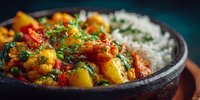Spicy vegetable curry with potatoes and herbs served alongside fluffy white rice in rustic bowl, ready for healthy dinner meal preparation.