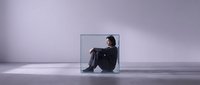 Young woman sitting in transparent glass cube against purple gradient background expressing isolation and confinement in minimalist surreal space.