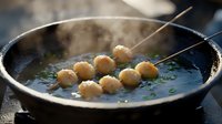 Steaming hot soup with homemade dumplings on skewers in cast iron pan, garnished with fresh herbs. Steam rising creates moody atmospheric food photography.