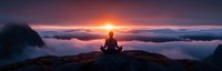 Silhouette of person meditating on mountain peak above clouds during dramatic sunrise, panoramic view showing tranquil mindfulness moment in nature.
